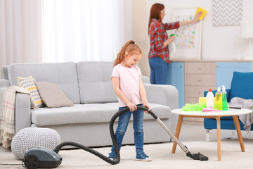 Little girl using vacuum cleaner while helping mother at home