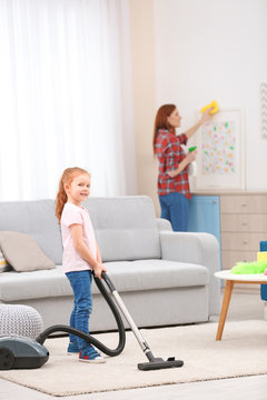 Little girl using vacuum cleaner while helping mother at home