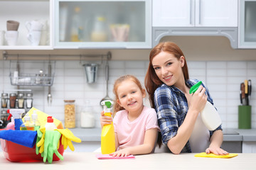 Little girl and her mother cleaning counter in kitchen at home