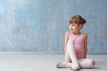 Cute little ballerina sitting on floor in dance studio