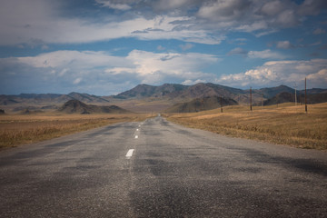 Road through a field of autumn grass on a background of high mountains