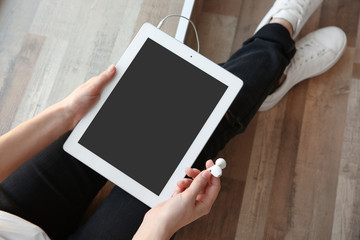 Audio book concept. Young woman holding tablet and earphones, close up