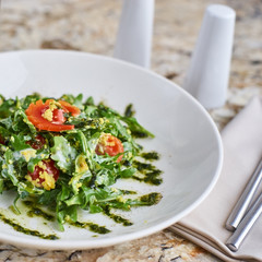 Salad with couscous, cherry tomatoes, avocado and mozzarella served on white plate. Salt shaker, pepper-castor and knife and fork on napkin on marble table