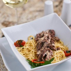 Beef stroganoff with spaghettini served in stylish square bowl on marble table