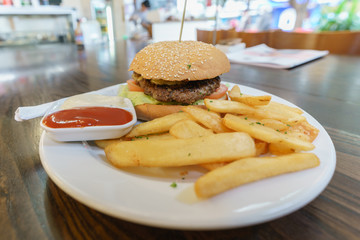 Delicious homemade recipe beef hamburger served with french fries , ketchup and mayonnaise on white plate on wood table