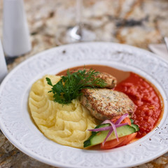 Chicken breast cutlets with mashed potatoes served with mushroom and tomato sauces on white plate on marble table