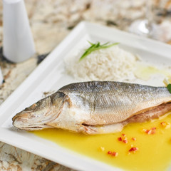 Whole boiled wolffish served with sauce from lemon butter and white wine on square white plate