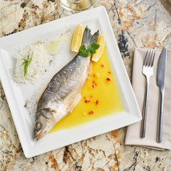 Whole boiled wolffish served with sauce from lemon butter and white wine on square white plate