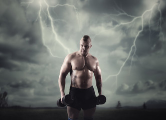 Fototapeta na wymiar Athlete with dumbbells, lightning in dark sky