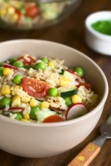 Bunter Vollkornreissalat mit Kirschtomaten, Mais, Gurke, Radieschen und Erbsen serviert in Schüssel, fotografiert mit natürlichem Licht (Selektiver Fokus, Fokus in die Mitte des Salats)