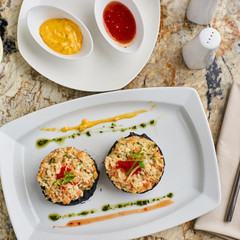 Crab cutlets with mashed potatoes with cuttlefish ink and spicy sauce served on white plate with glass of white wine on marble table