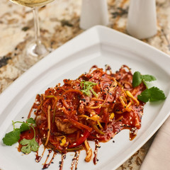 Spicy tofu served on white plate with glass of white wine on marble table. Vegeterian cuisine.