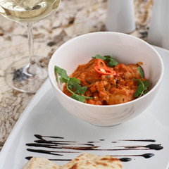 Chicken fillet slices fried in spicy cream sauce with tortilla bread served in white bowl with glass of wine, knife and fork on napkin on marble table
