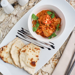 Chicken fillet slices fried in spicy cream sauce with tortilla bread served in white bowl with glass of wine, knife and fork on napkin on marble table