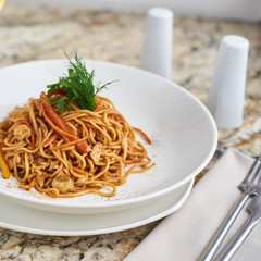 Flat egg noodles with vegetables served in big white ceramic round plate with glass of white wine on marble table