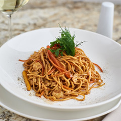 Flat egg noodles with vegetables served in big white ceramic round plate with glass of white wine on marble table