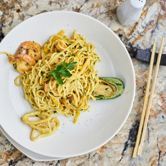 Flat egg noodles with seafood served in big white ceramic round plate with glass of white wine on marble table