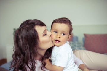 Young mom and young son sitting on the bed. Mom plays with her son. Family.