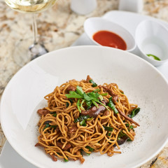 Flat egg noodles with duck meat, chicken, shiitake mushrooms served on white plate with white garlic and red spicy sauce