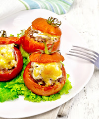 Tomatoes stuffed with meat on lettuce in plate on light board