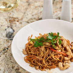 Thin egg noodles with chicken slices served on white plate with white garlic and red spicy sauce