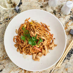 Thin egg noodles with chicken slices served on white plate with white garlic and red spicy sauce