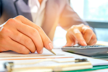 Businessmen using a calculator and a pen to analyze data from the graph on the desk.