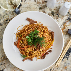 Thin egg noodles with beef meat slices served on white plate with white garlic and red spicy sauce
