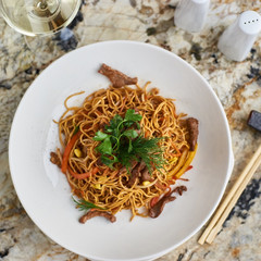Thin egg noodles with beef meat slices served on white plate with white garlic and red spicy sauce