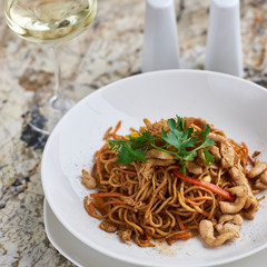 Thin egg noodles with chicken slices served on white plate with white garlic and red spicy sauce