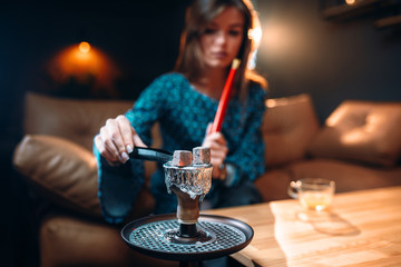 Young woman holds coal with tongs, smoking hookah