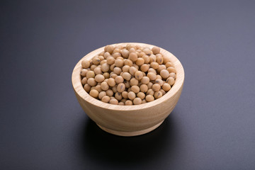 Soybeans in a wooden bowl and soybean oil on a black background