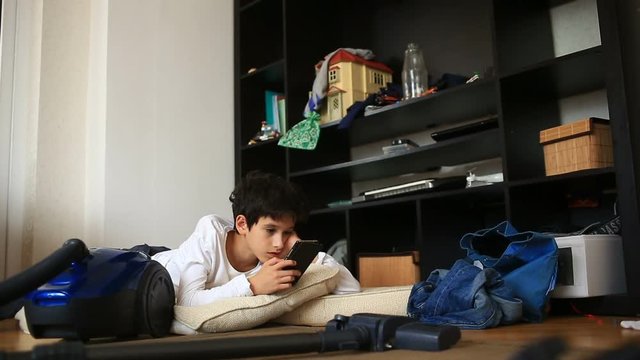 Boy teenager is shirking her homework, playing on her mobile phone. Cleaning of the children's room. Disorder in the teen room