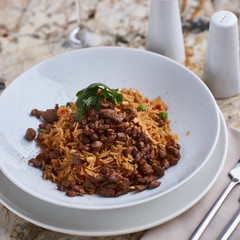 Fried rice with beef slices served in white round plate with glass of white wine on marble table