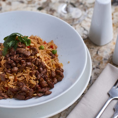 Fried rice with beef slices served in white round plate with glass of white wine on marble table