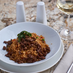 Fried rice with beef slices served in white round plate with glass of white wine on marble table