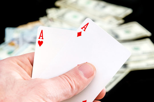 Man's hand holding two aces on dollars background.