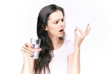 woman examines a pill, a glass of water