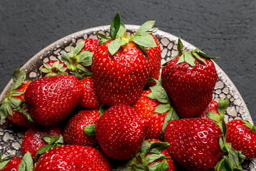 fresh ripe useful fruit strawberry in a clay bowl closeup on a black background
