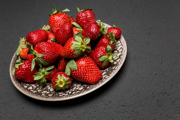 fresh ripe useful fruit strawberry in a clay bowl closeup on a black background