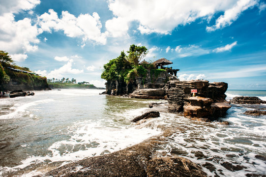 Pura Tanah Lot. Unique hindu temple on a rock in the sea, Bali, Indonesia. Wide angle, dramatic sky with clouds and waves and swash in the foreground.