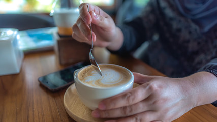 Hand holding a spoon stirring a cup of hot cappuccino coffee