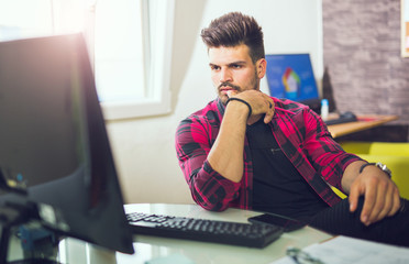 Handsome caucasian man at work desk facing flat screen computer screen in office