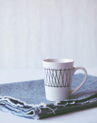 Hot drink in white patterned mug on blue jeans fabric and grey background