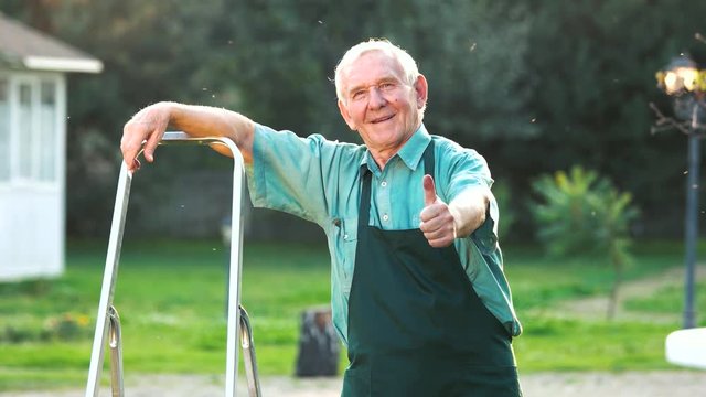 Old gardener showing thumb up. Happy man in apron. Successful gardening business.