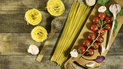 Italian pasta, cherry tomatoes, garlic, mushrooms and spices on a rustic wooden table.