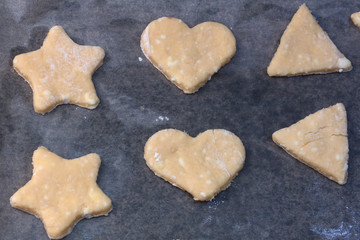 Cookie dough in different shapes lies on the baking sheet.