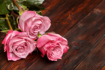 Three beautiful pink roses on wooden table, romantic background