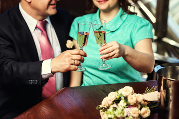 Womans and mans wedding hands with glasses.Happy newlyweds couple drink white wedding champagne wine.New family,husband and wife celebrate engagement