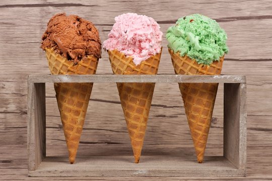 Chocolate, Cherry And Pistachio Ice Cream In Waffle Cones In Rustic Holder Over A Wood Background